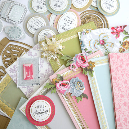 A variety of papers and embellishments from the Paper Shoes Finishing School Craft Box are carefully arranged on a table.