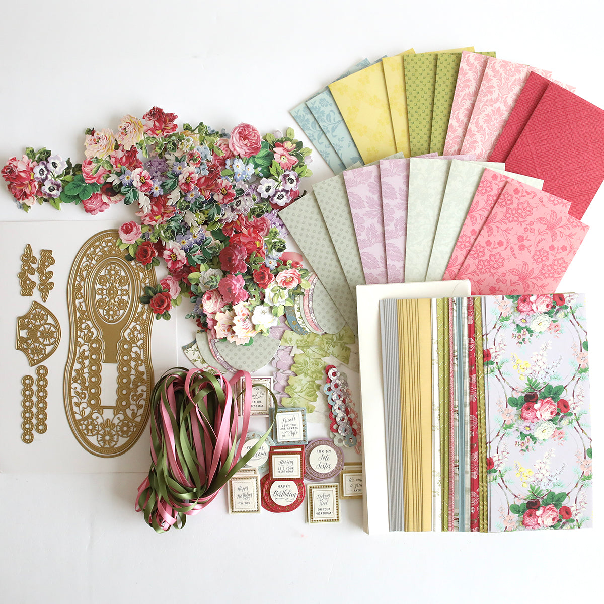 An assortment of 2024 Finishing School Craft Box Autoship materials including patterned papers, floral embellishments, stickers, and paper shoes laid out on a white surface.