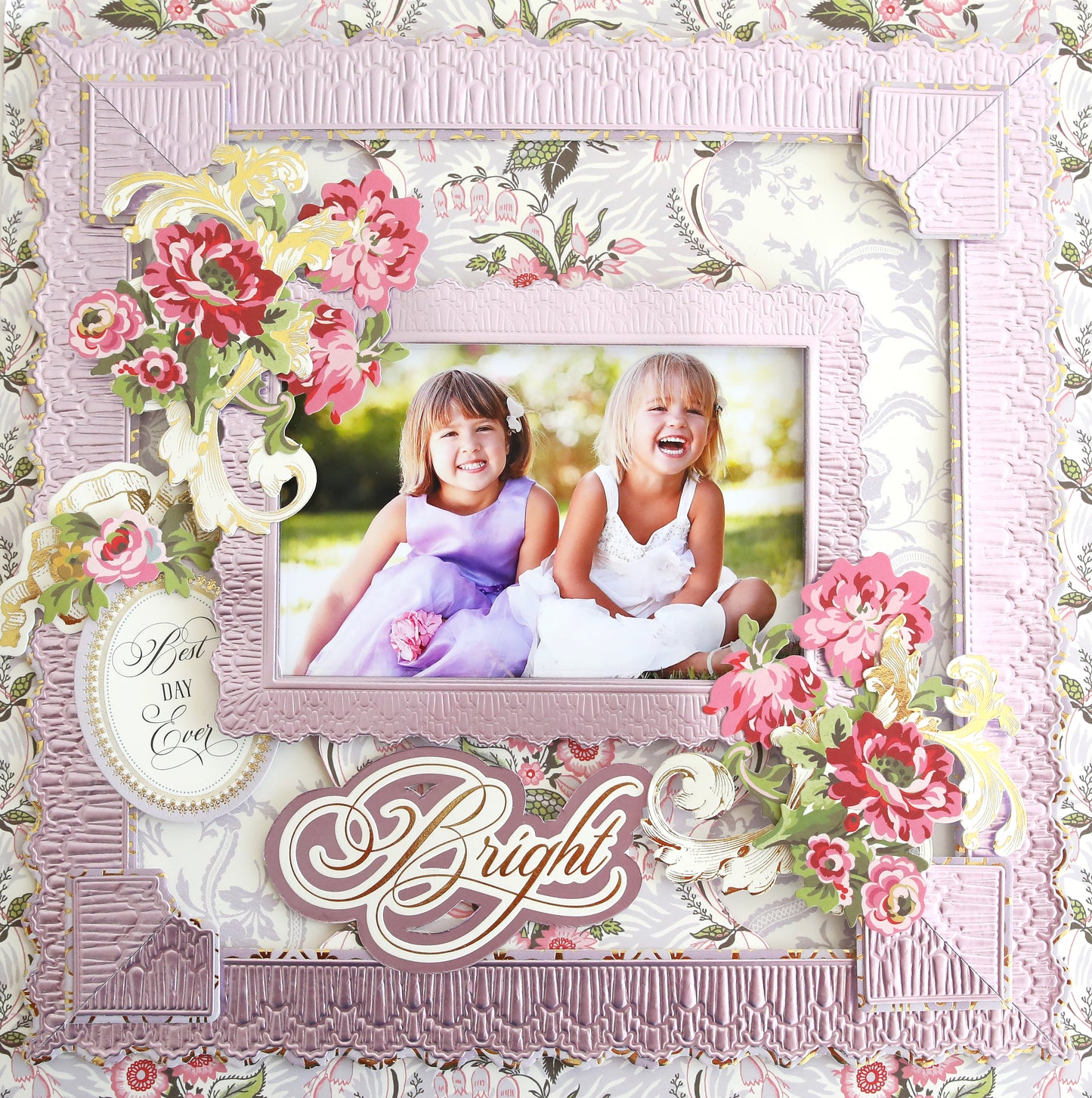 Two young children sit on grass, laughing, in a framed photograph surrounded by pink floral decorations and various scrapbook supplies with the words "Phoebe Papers and Embellishments" at the bottom.