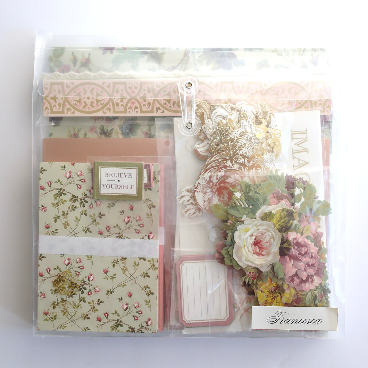 The Crop at Home 5 Ultimate Materials Kit includes a clear plastic folder with floral scrapbook stationery, decorative cardstock, flower die-cuts, and labels such as "Believe Yourself" and "Francesca.