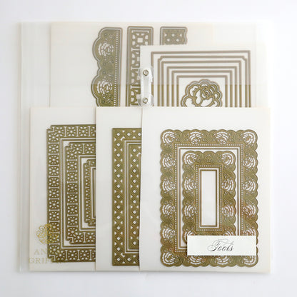 The Crop at Home 5 Ultimate Materials Kit features ornate gold metal cutting dies and matching white cardstock samples, neatly arranged on a white background—perfect for scrapbook enthusiasts.