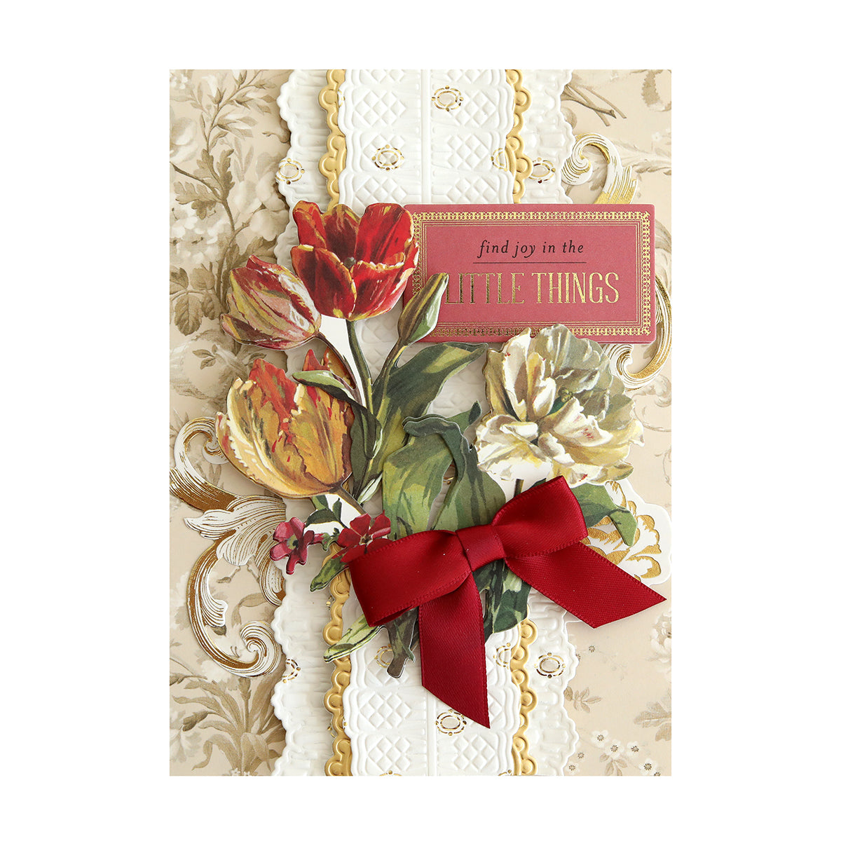 A greeting card with floral artwork, featuring red and white flowers, a red ribbon, and a message reading, "find joy in the little things" on a beige ornate background.