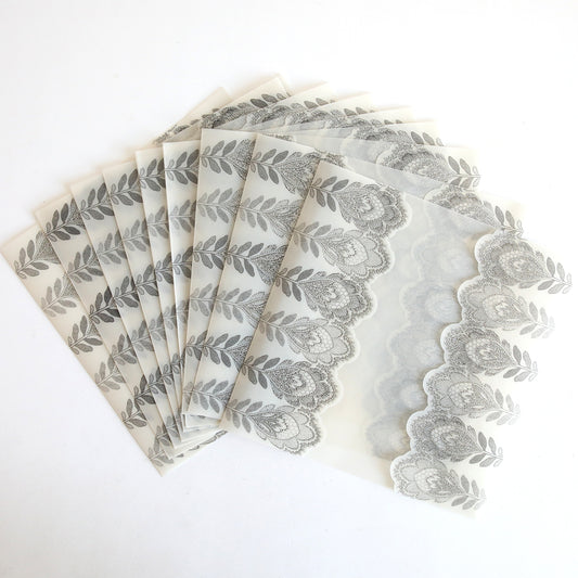 Ten Silver Glitter Feather Vellum Gatefold envelopes, perfect for wedding invitations, are elegantly fanned out on a white background.