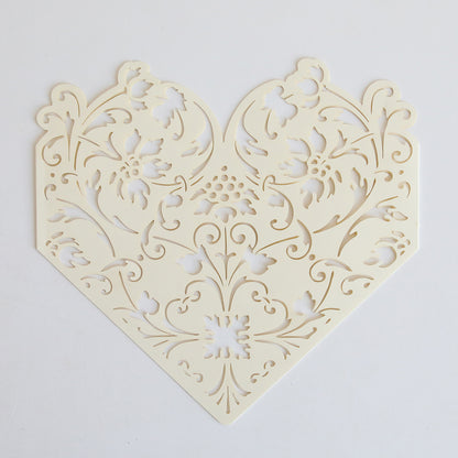 The Ivory Diecut Heart Sleeve 10 pack features intricately cut, cream-colored sleeves with a symmetrical floral heart design, perfect for elegant wedding invitations. Set of 10, shown on a plain white background.