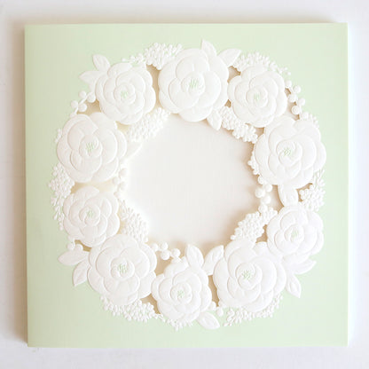 The Floral Wreath Laser Cut Square 10 pack features pale green square cards with a detailed, white embossed floral wreath in the center, perfect for custom invitations.