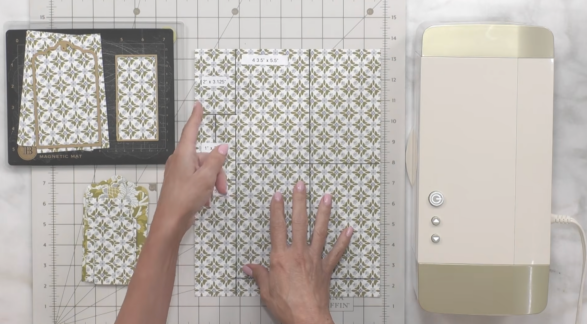 A person arranges patterned paper on a cutting mat next to a buttoned machine, likely prepping for a craft inspired by Anna Griffin | Create Fall 2026.