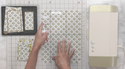 A person arranges patterned paper on a cutting mat next to a buttoned machine, likely prepping for a craft inspired by Anna Griffin | Create Fall 2026.