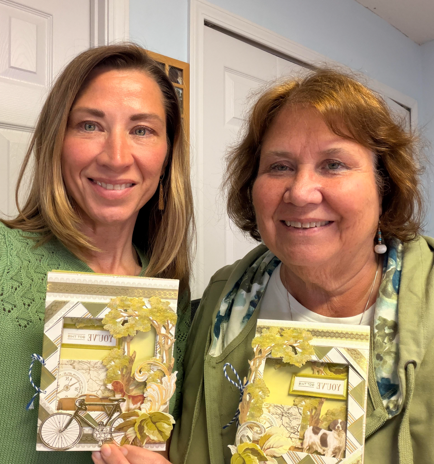 Two women smile indoors, holding handmade cards with green and yellow designs, capturing the vibrant spirit of their craft class with Anna Griffin | Create Fall 2026.