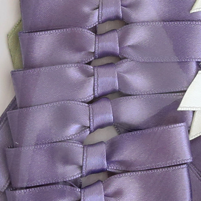 Small Pre-Tied Bows in lavender satin are neatly overlapped on a flat surface, ideal for mixing with green, blue, purple, ivory, or gold bows from a 50-piece set.