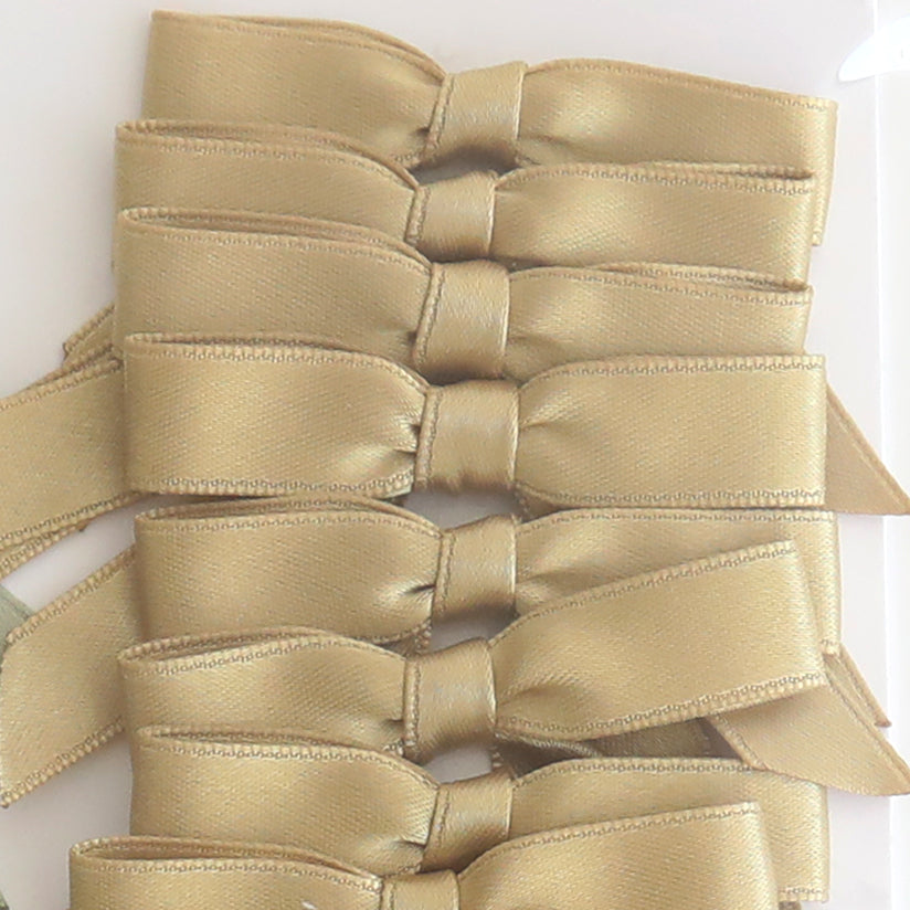 Six Small Pre-Tied Bows in golden satin are neatly stacked vertically on a white surface, ideal for adding an elegant touch to any project.