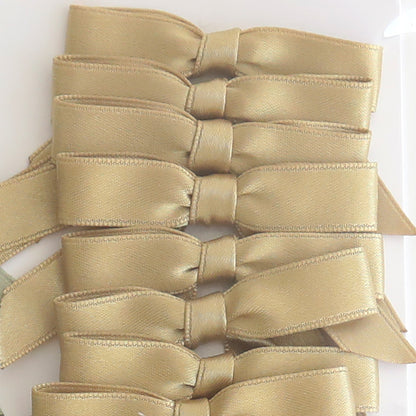 Six Small Pre-Tied Bows in golden satin are neatly stacked vertically on a white surface, ideal for adding an elegant touch to any project.