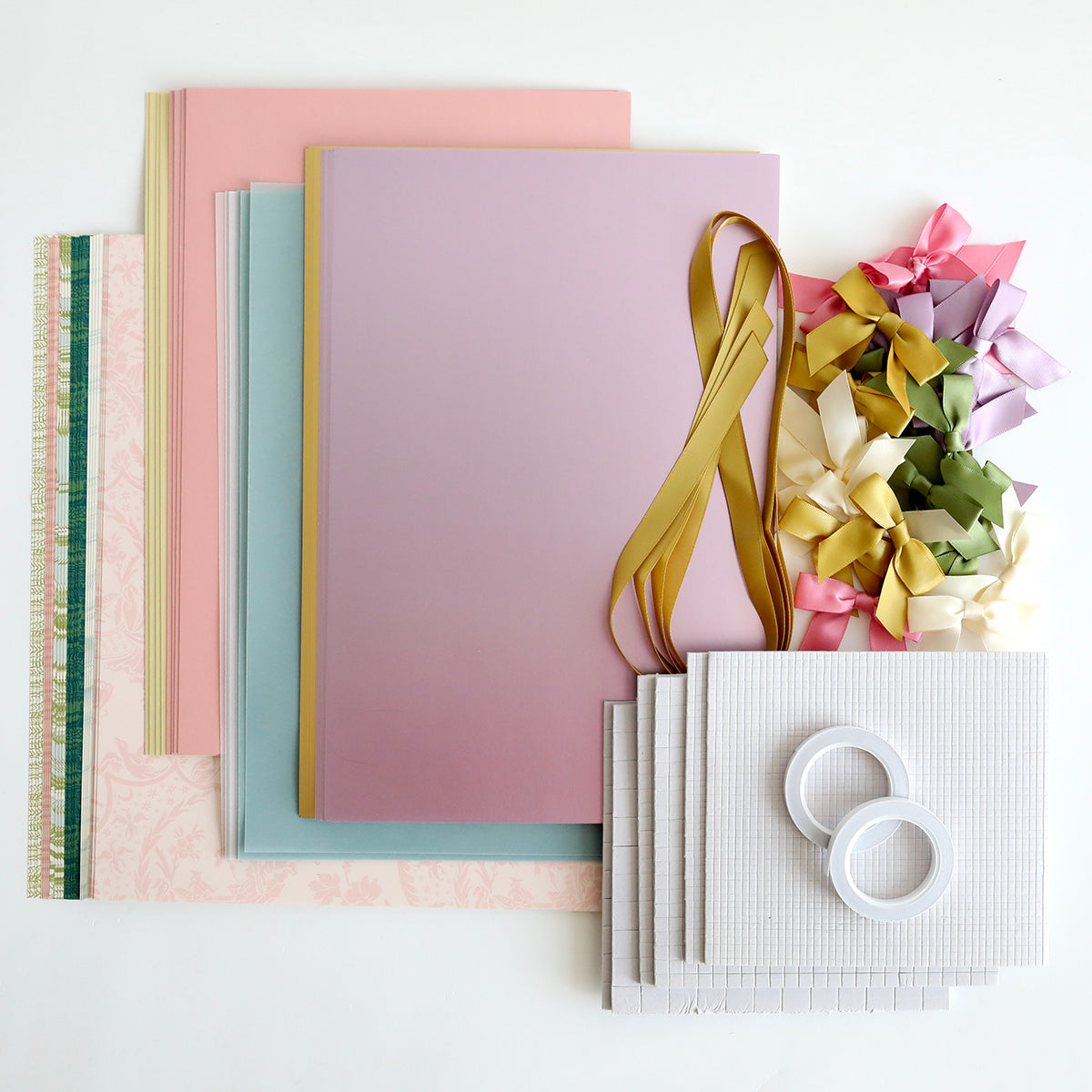 Crop at Home 5 Swag Materials, including premium pastel papers, ribbons, bows, two tape rolls, and textured sheets, are arranged on a white surface.