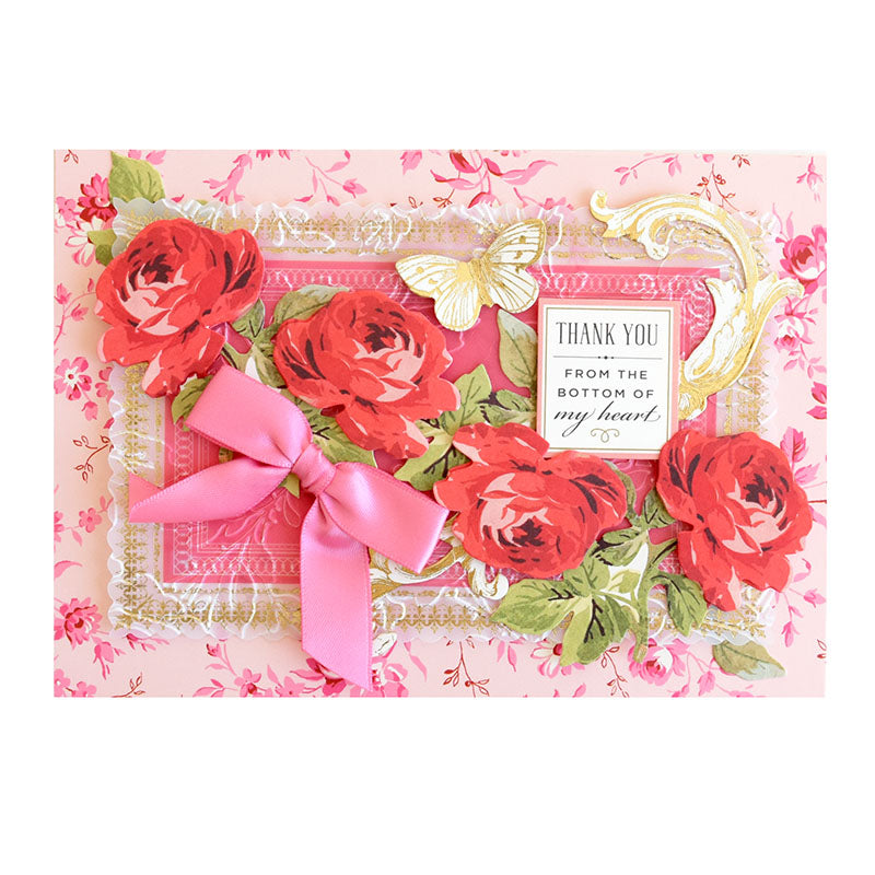 A pink floral Thankful Sentiments and Floral Stickers greeting card decorated with red roses, a pink ribbon, a gold butterfly, and sentiment rub-ons reading “THANK YOU FROM THE BOTTOM OF my heart.”