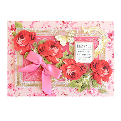 A pink floral Thankful Sentiments and Floral Stickers greeting card decorated with red roses, a pink ribbon, a gold butterfly, and sentiment rub-ons reading “THANK YOU FROM THE BOTTOM OF my heart.”
