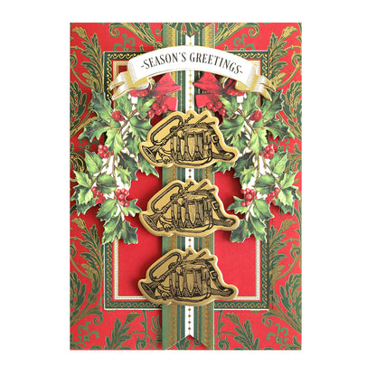 A festive card with red, green, and gold holly design, featuring a "Season's Greetings" banner and three sleigh illustrations in the center, adorned with Anniversary Christmas Stamps & Dies.