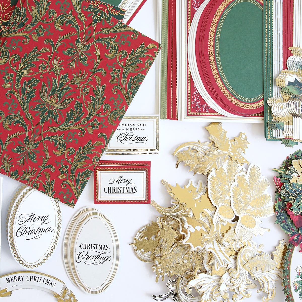 Collection of Christmas-themed paper crafts, including red and green patterned papers, gold decorative cutouts, and the Christmas Greetings Card Making Kit featuring festive greeting cards with messages like "Merry Christmas" and "Christmas Greetings.