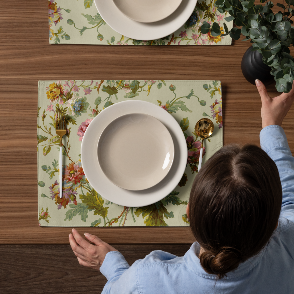 Someone arranges eucalyptus in a black vase on a wooden table set with a Placemat Set of 4, white plates, and gold cutlery.