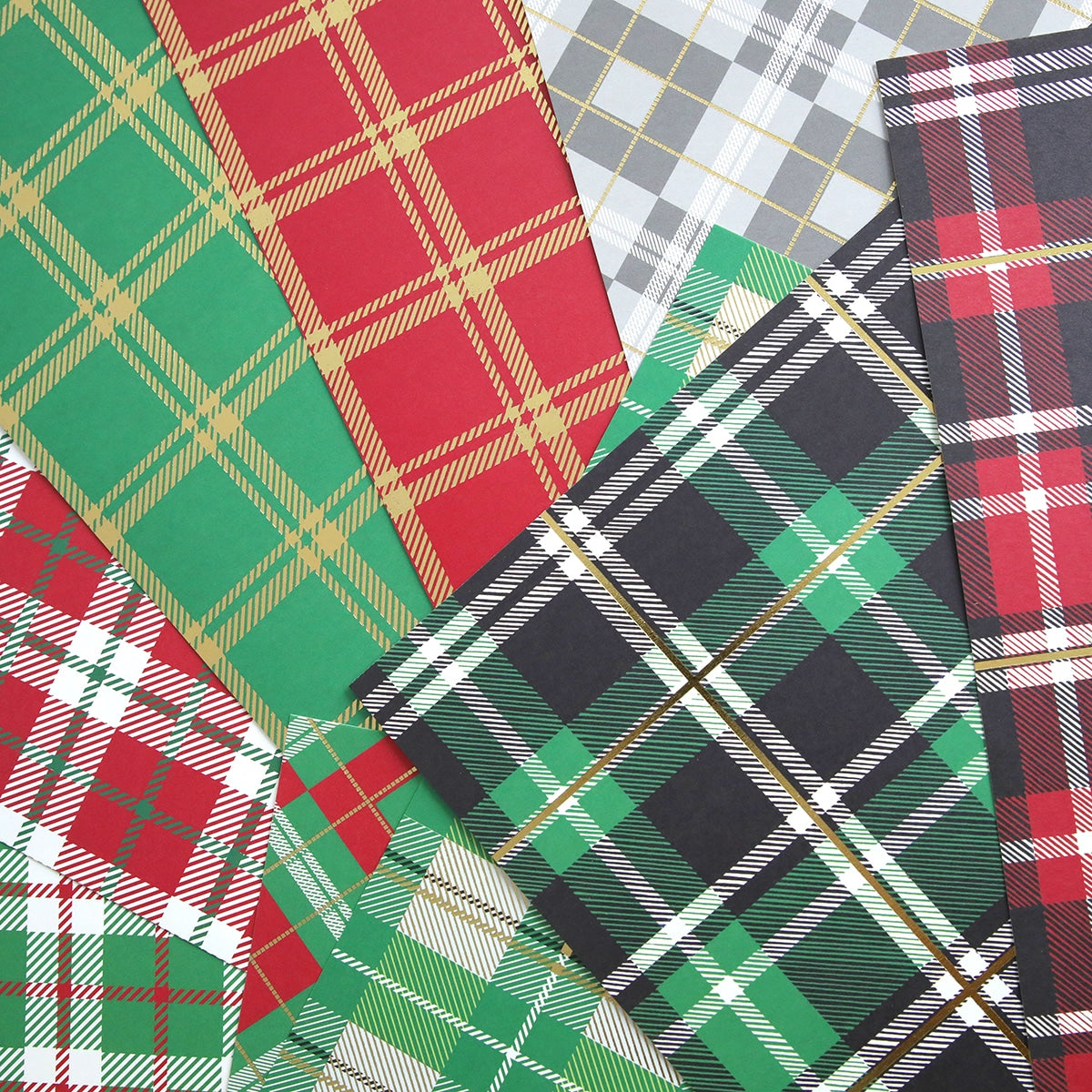 a pile of Christmas Plaid 12x12 Cardstock papers on a white surface.