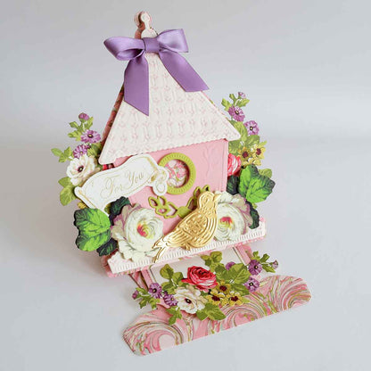 a pink birdhouse with a purple bow on top of it.