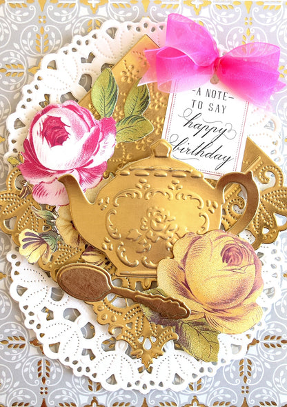 a close up of a card with a teapot and flowers.