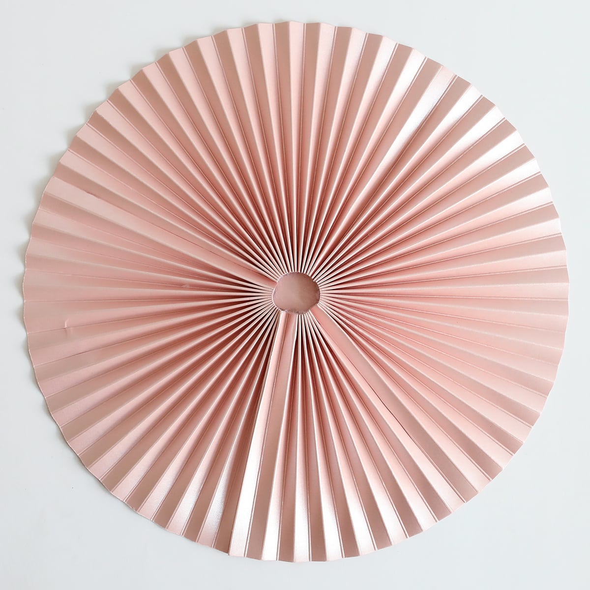 a pink paper fan sitting on top of a white wall.