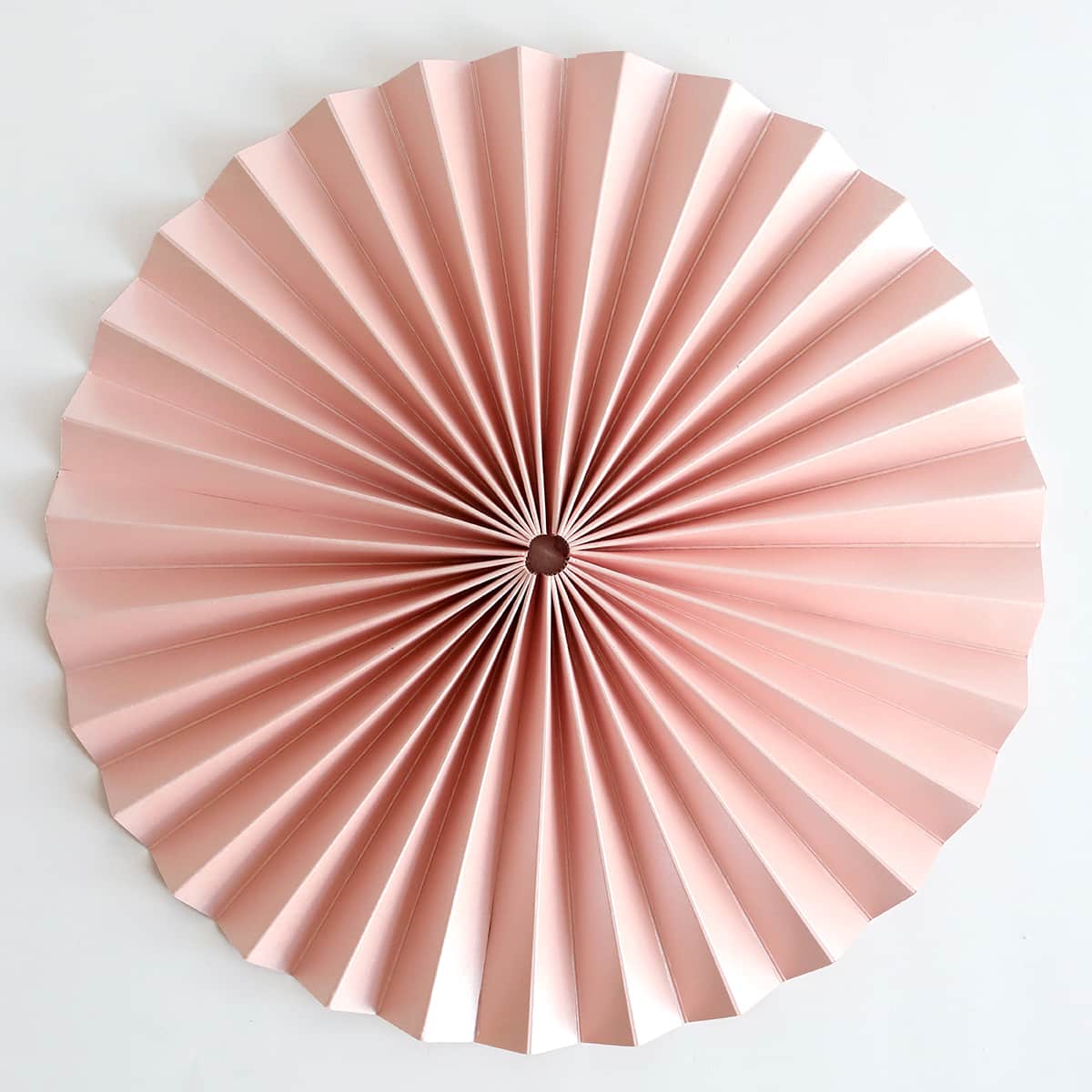 a pink paper fan on a white wall.