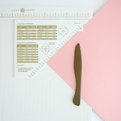 A pink Scoring Board with Corner Punch and Cardstock and a knife.